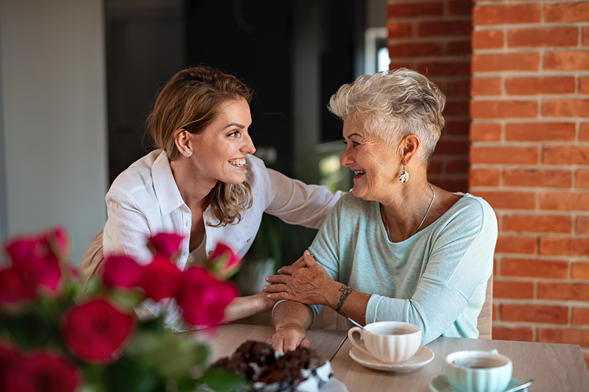 Happy senior mother having coffee with adult daughter indoors at home, sitting and talking.