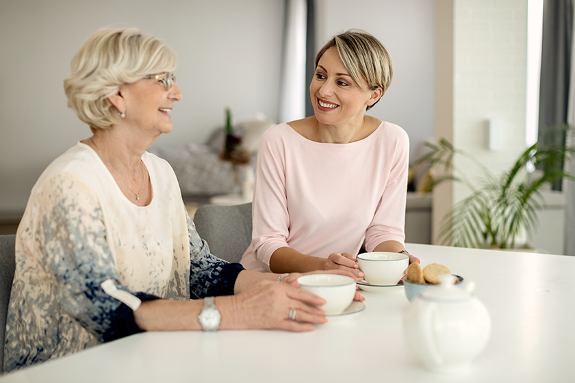 Happy woman and her senior mother talking while drinking coffee at home. 