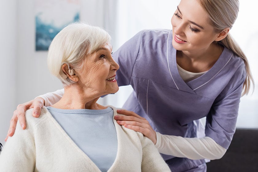 Smiling social worker hugging shoulder of senior woman with hearing aid