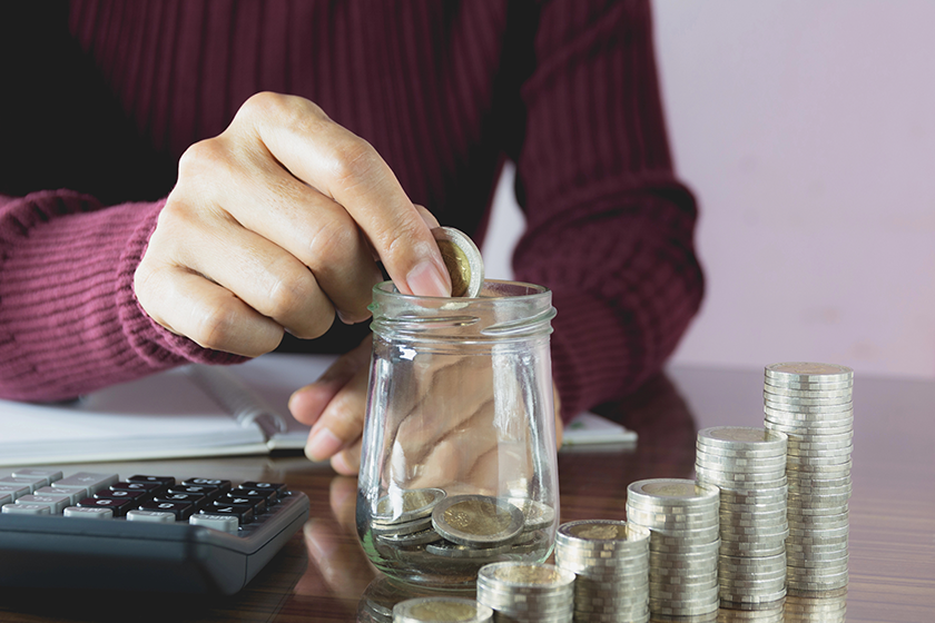 Woman process and drop coin into the glass with stack coins and calculator. Woman working on table. 